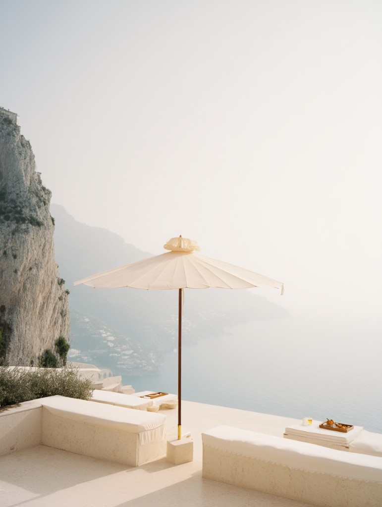 Cliffside terrace with a cream parasol overlooking a hazy Mediterranean coastline